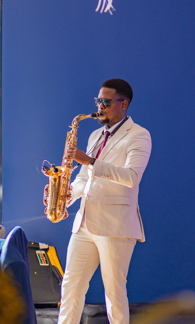 Ian Miako playing a gold alto saxophone in a cream suit and sunglasses at a corporate event