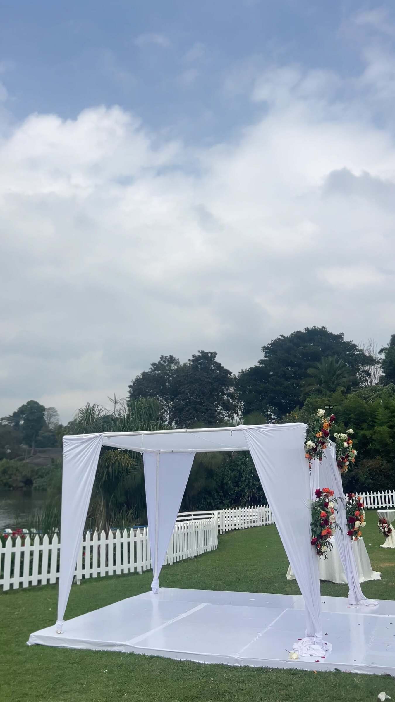 Ian in a burgundy suit playing saxophone on a lakeside lawn as a wedding ceremony is set up